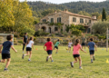 Imagen de una casa de colonias de piedra en la naturaleza con un campo de futbol y juegos de equipo con escolares corriendo juntos