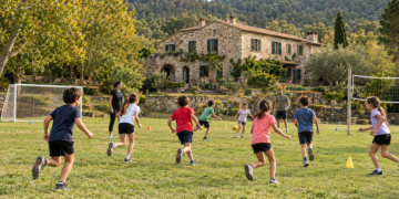 Imagen de una casa de colonias de piedra en la naturaleza con un campo de futbol y juegos de equipo con escolares corriendo juntos