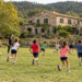 Imagen de una casa de colonias de piedra en la naturaleza con un campo de futbol y juegos de equipo con escolares corriendo juntos
